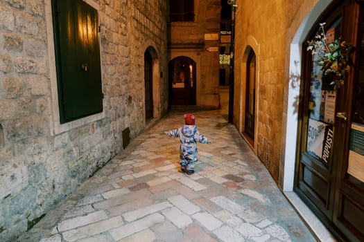 Little girl walks along the cobbled street of an old town in the light of lanterns. Back view. High quality photo