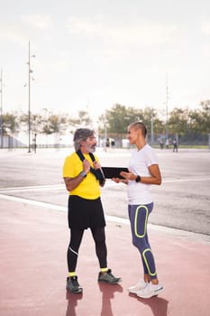 female personal trainer showing training on a tablet to a senior sports man, concept of healthy and active lifestyle in middle age, copy space for text