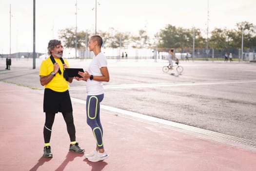 female personal trainer showing training on a tablet to a senior sports man, concept of healthy and active lifestyle in middle age, copy space for text