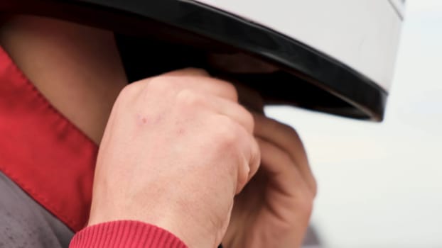 Extreme close up of a man trying to take off white protective helmet on bright sky background. Young man is trying to unfasten his safety helmet to take it off.
