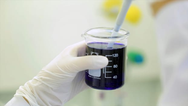 Close-up of glassware with blue fluid in scientist hand during medical test. Hands of clinician holding steel tools during scientific experiment in laboratory. test tubes and dropper.