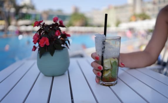 Female hand holding alcoholic cocktail with ice mojito closeup. Carefree hotel stay concept