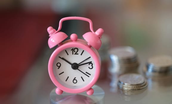 Pink alarm clock compass and stacks of coins. Credit success and growing money back concept