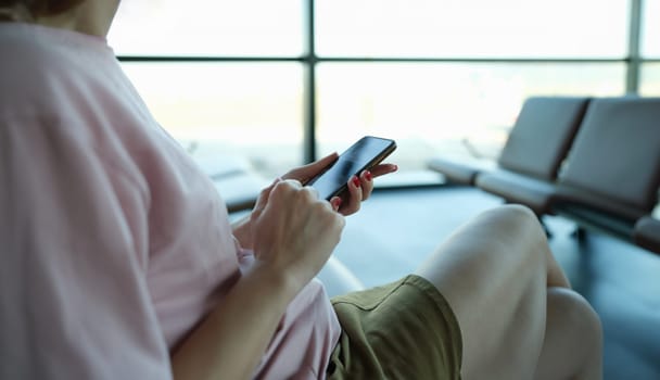 Woman typing message on mobile phone in airport building closeup. Travel mobile app concept