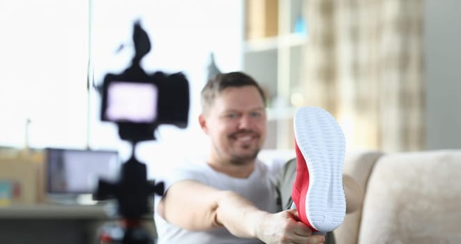 Cheerful male blogger calls red sneakers while recording new video for blog. Overview of sports shoes concept