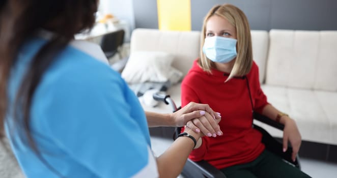 Rehabilitation doctor in protective medical mask communicates with disabled woman in wheelchair. Rehabilitation and treatment in hospice concept