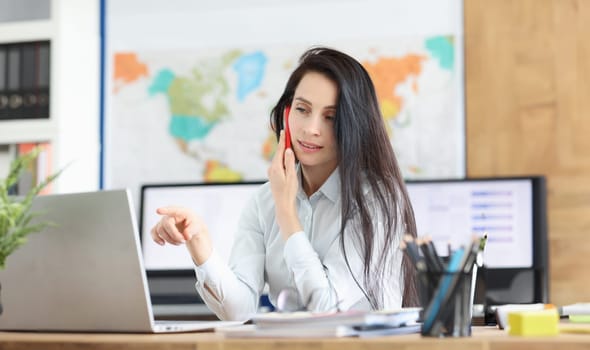 Business consultant positively talking on mobile phone working on laptop in office. Secretary enjoying work process and talking on smartphone concept
