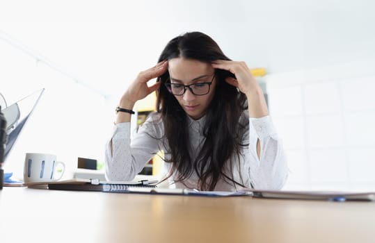 Tired sleepy woman sits at table holds head and rests at the workplace. Bored young woman feeling sleepy lazy and unmotivated at work