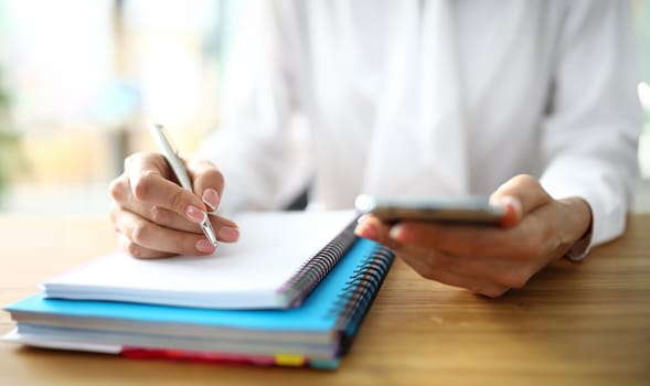 Closeup of freelancer hands with mobile phone working on finance. Student studying online at home and working from home.