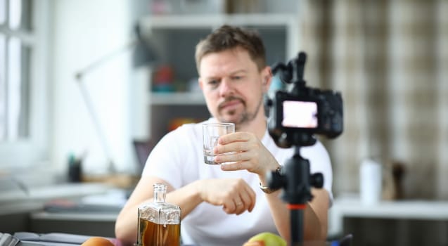 Exhausted man with black eye drinks alcohol in front of camera. Loneliness and alcoholism blogger concept