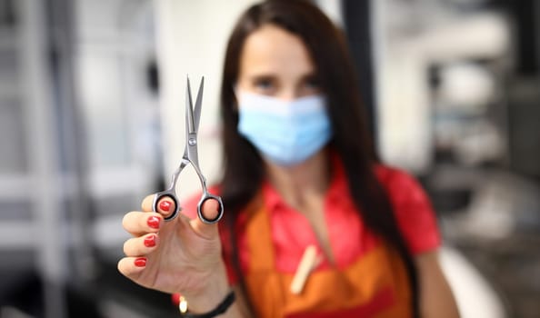 Woman hairdresser in protective mask holds scissors. Health safety and provision of services in beauty salon