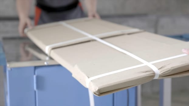 Close-up of workers packed flat package. Action. Workers in overalls pack building material from factory for home delivery. Building materials or furniture are delivered directly from factory.