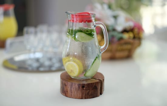 Glass jug of detox water with lemon and cucumber standing on table closeup. Healthy food concept