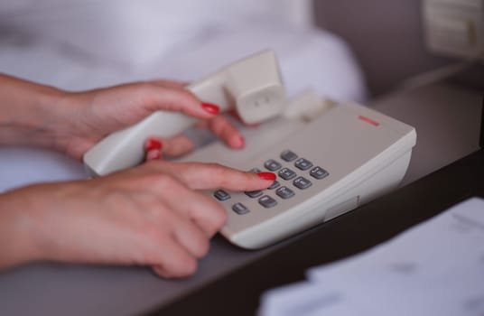 Female hands with red manicure dialing phone number closeup. Hotel service concept