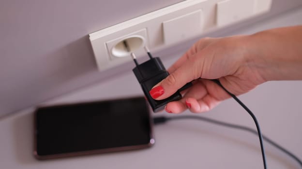 Woman hand plugging mobile phone charger into socket closeup. Fast charging smartphones concept