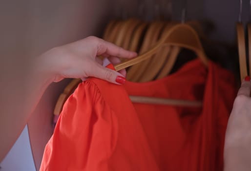 Female hand choosing red dress on hanger closet closeup. Special occasion clothing concept
