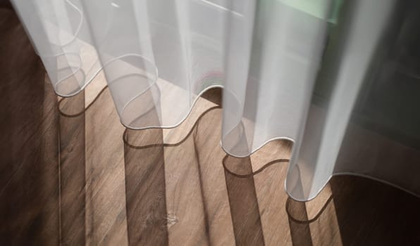 Sunlight falling on wooden floor and creating shadow from curtains background. Interior design sewing curtains concept