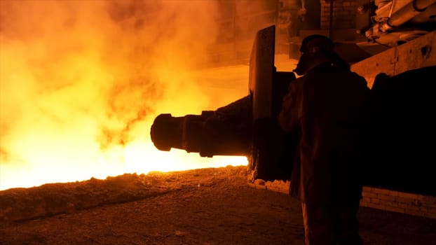Steel worker near the molten metal flowing in the chute. Metallurgical equipment and technology of iron production. Blast furnace.