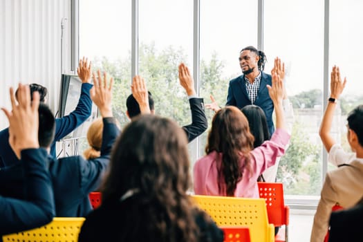 Engaged in a strategy session businesspeople gather in a boardroom for a meeting and seminar. Questions are posed with hands raised by colleagues and employees showcasing teamwork.