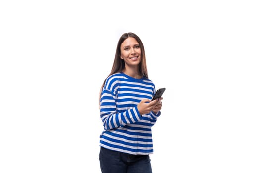 pretty young slim european model woman dressed in a blue sweater holding a smartphone in her hand on a white background.