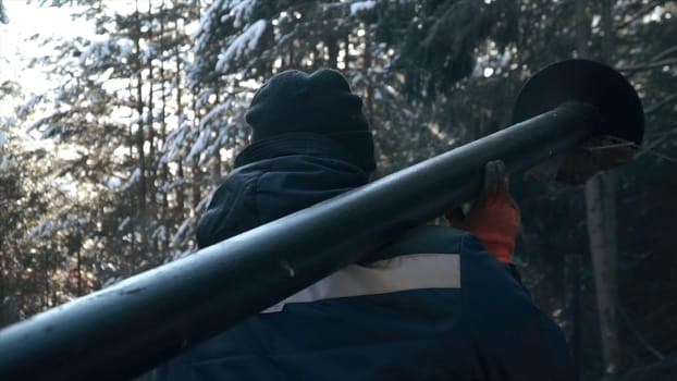 Worker carries lamppost. Clip. Workers install lamppost in wooded park. Installing lamppost in park in winter. Man carries steel pole.