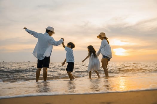 Silhouette of family holding hands live healthy lifestyle on beach, Happy Asian family have fun jumping together on beach in holiday sunset time, Back people enjoying travel trip and summer vacations