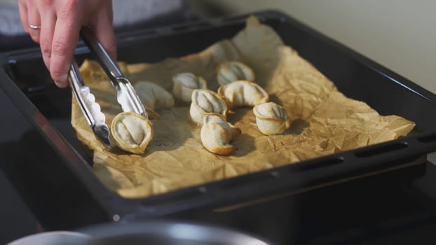 Dumplings baked on a pan. ART. The cook took one dumpling with tongs. Eight baked dumplings lie on a baking sheet and paper.