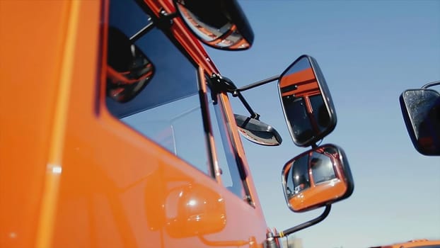 Close up of the side mirror and part of the truck body of red color on blue clear sky background. New truck details, construction concept.