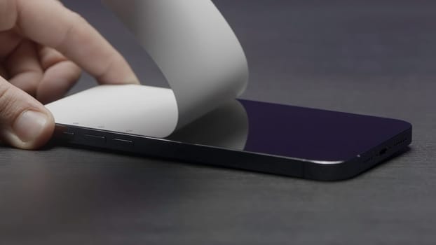 Close up of removing screen protector on the smart phone at a service center. Action. Male hands putting off a white film from the black smartphone screen