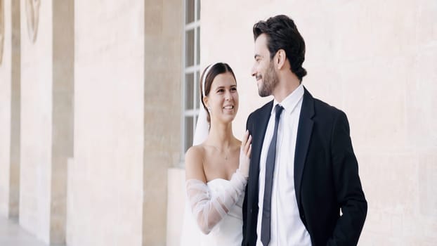 Newlyweds, caucasian bride and groom posing by the building outdoors. Action. Woman in white dress with a man in suit