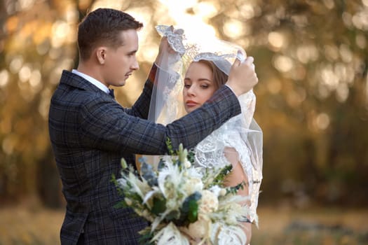 happy bride and groom enjoying romantic moments under veil outside on natural background in sunny day