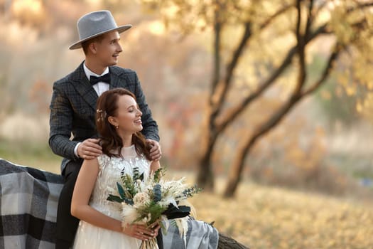 beautiful happy stylish bride and groom in hat laughing near tree in autumn