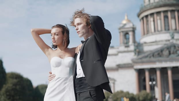 Beautiful newlyweds on background of old architecture. Action. Elegant couple of newlyweds posing on background of cathedral on sunny day. Newlyweds on windy sunny day in summer.