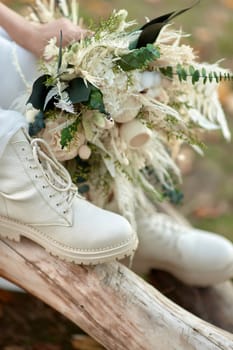 bride wearing white boots holding beautiful autumn bouquet.