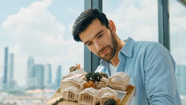 Businessman in casual outfit holding house model while checking house construction. Architect engineer inspect building model while standing near window with skyscraper. Engineering. Tracery
