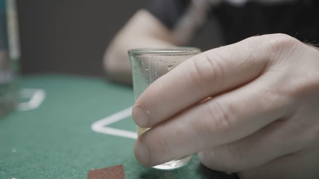Close-up of man drinking vodka. Action. Man drinks glass while playing poker. Russian bandit in black glasses drinks vodka and plays cards.