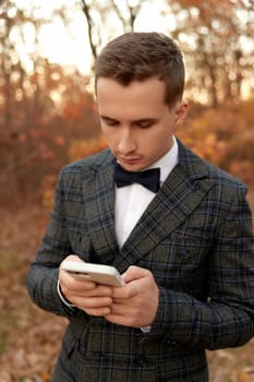 Handsome young man in classic checked suit using phone outdoor