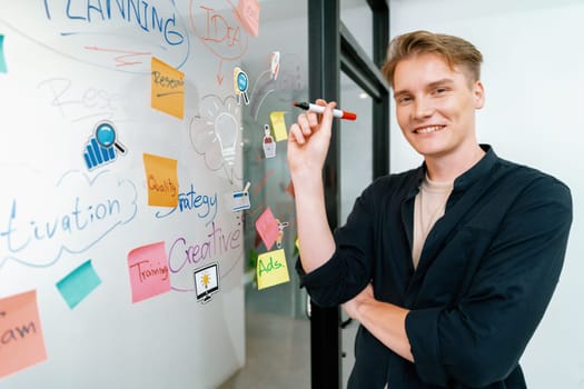 Professional caucasian male leader writing and sharing marketing idea by using mind map and sticky notes on glass board at modern meeting room. Creative business and planing concept. Immaculate.