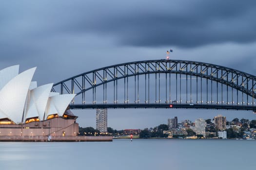 SYDNEY, AUSTRALIA - DECEMBER 03 2023: Sydney Opera House and Harbour Bridge at dusk during a summer storm from Mrs Macquarie's Chair in Sydney, New South Wales, Australia