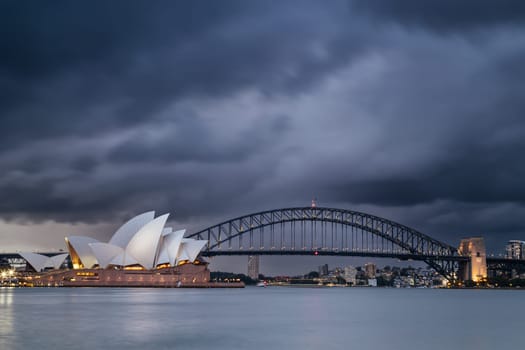 SYDNEY, AUSTRALIA - DECEMBER 03 2023: Sydney Opera House and Harbour Bridge at dusk during a summer storm from Mrs Macquarie's Chair in Sydney, New South Wales, Australia