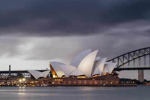 SYDNEY, AUSTRALIA - DECEMBER 03 2023: Sydney Opera House and Harbour Bridge at dusk during a summer storm from Mrs Macquarie's Chair in Sydney, New South Wales, Australia