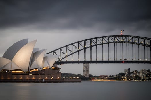 SYDNEY, AUSTRALIA - DECEMBER 03 2023: Sydney Opera House and Harbour Bridge at dusk during a summer storm from Mrs Macquarie's Chair in Sydney, New South Wales, Australia