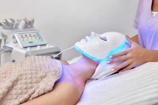 woman receiving led light anti-aging mask treatment from beautician in beauty salon