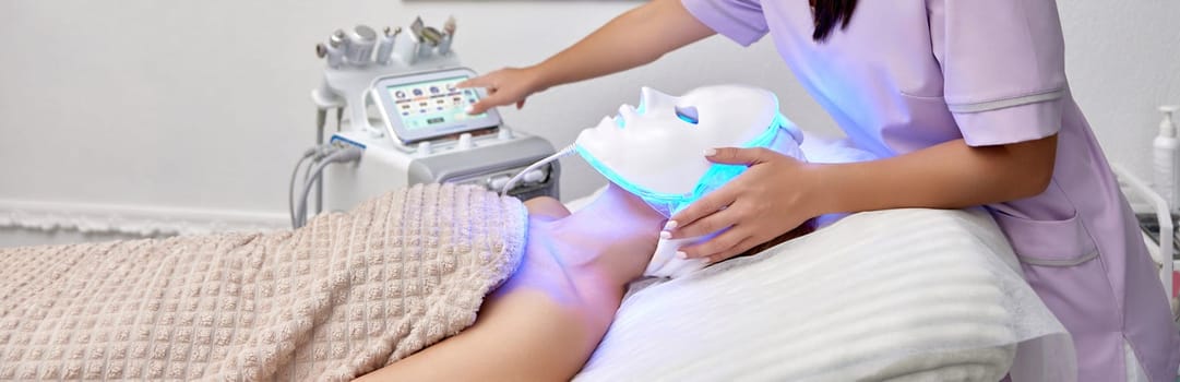 woman receiving led light therapy mask treatment from beautician in beauty salon