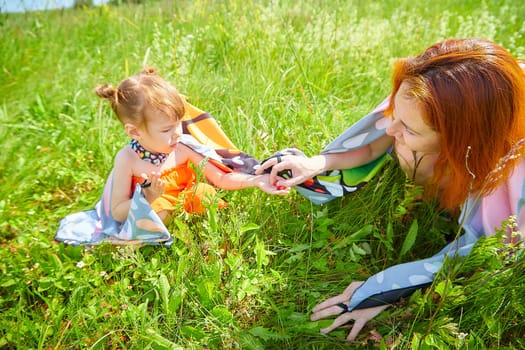 Happy female family with mother and daughter on green and yellow meadow full of grass and flower. Woman with red hair and blonde girl having fun, joy and hug in sunny summer day. Concept family love