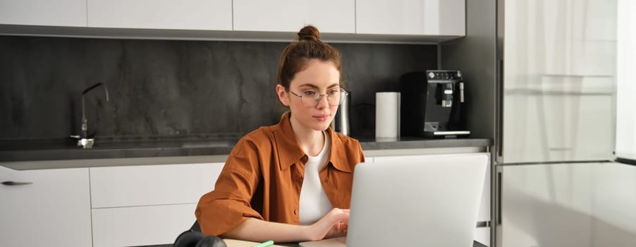 Portrait of young concentrated woman in glasses, self-employed freelancer, working from home on laptop, using computer at home.