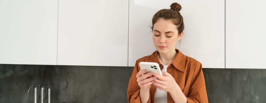 Lifestyle shot of young beautiful woman at home, looking at her mobile phone screen, typing, checking social media, reading a message or news feed on smartphone.