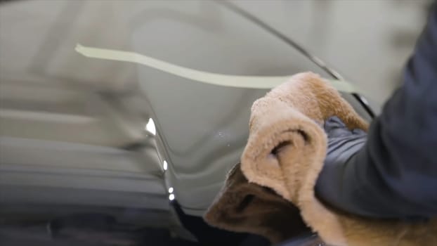 Close up for man hand in black glove washing a car window in a car wash, cleaning service. Car care service worker using microfiber cloth for cleaning a car.