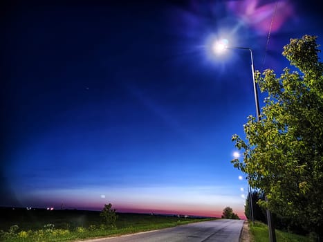 Asphalt road at night with lanterns on the side of road and the natural landscape around