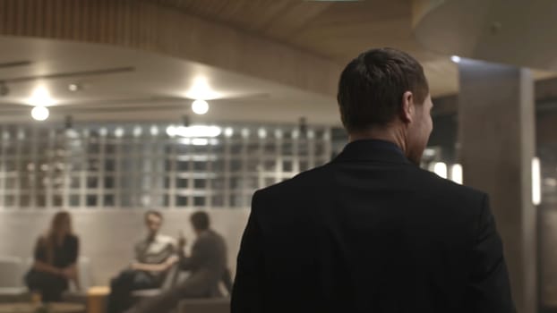 Walking Man in Suit, Back View, blurred background. A man in a suit walks across a work loung - closeup from behind. Blurred, defocused man walks down the hallway.